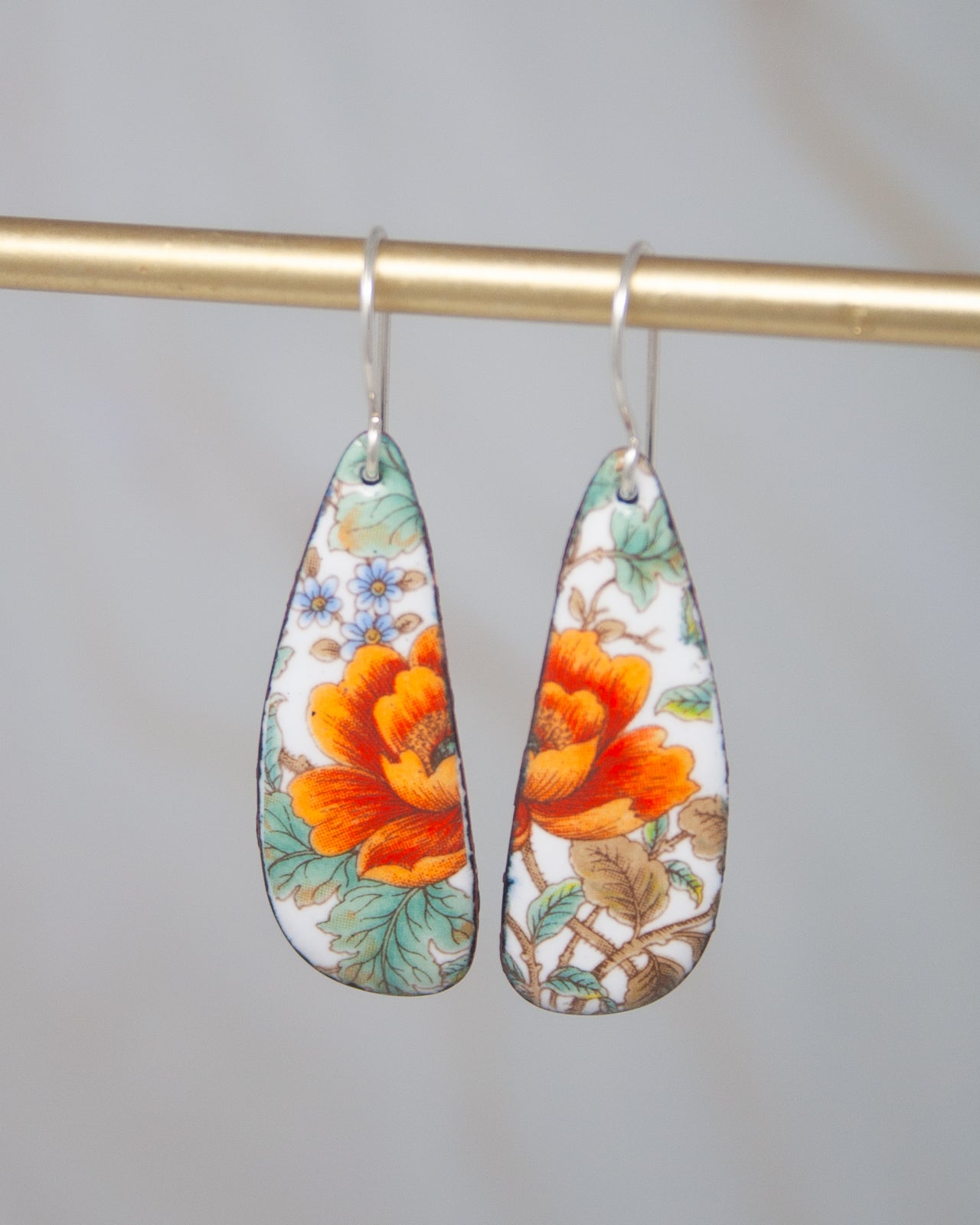 A pair of earrings with a floral design, featuring a large orange flower and green leaves.