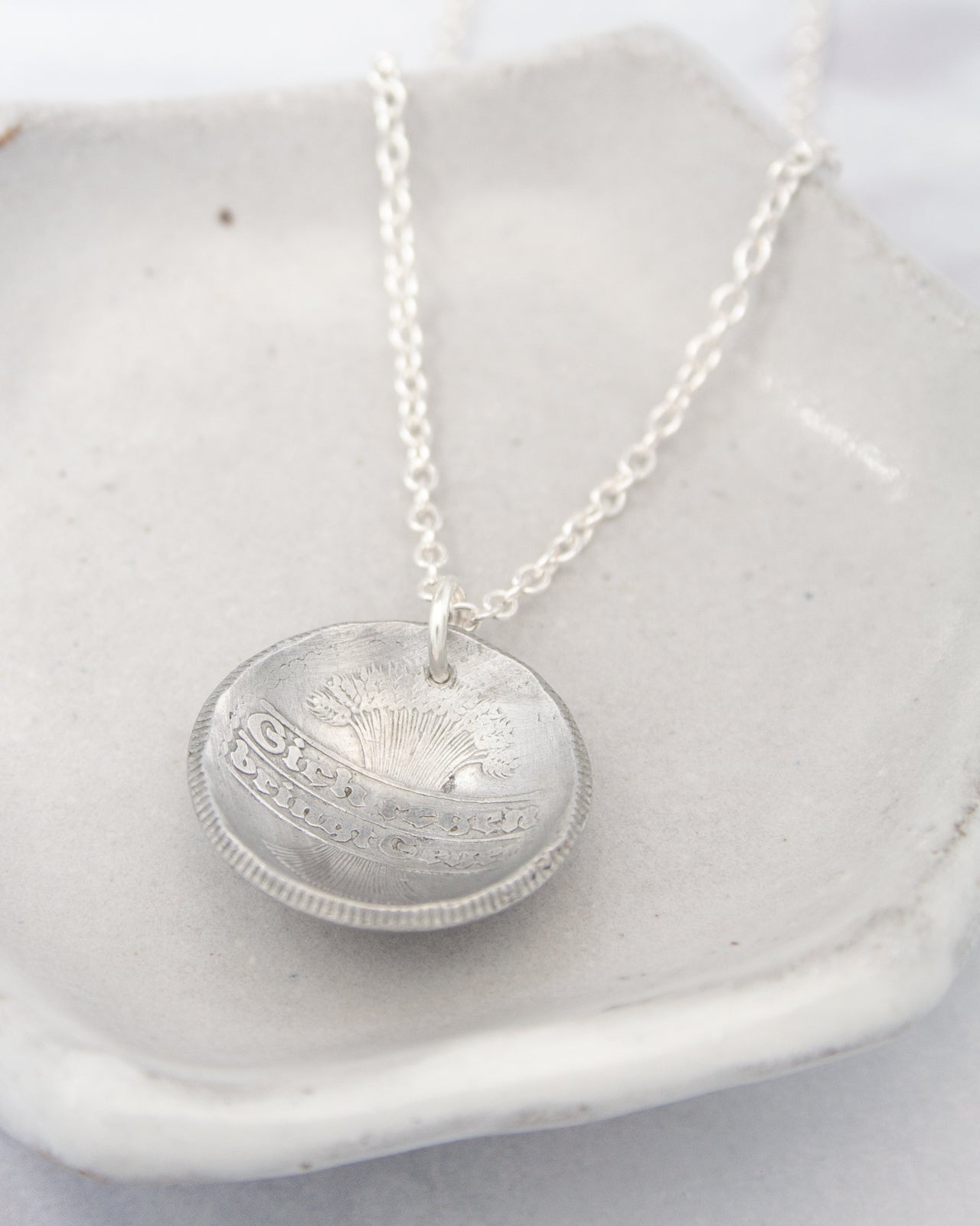 A silver necklace with a pendant featuring a design on it, resting on a white surface.