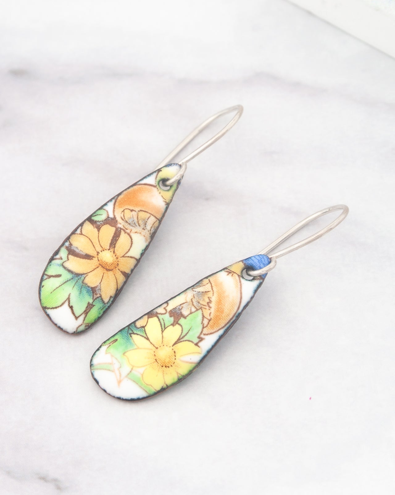 A pair of earrings with a floral design, featuring yellow flowers and green leaves.