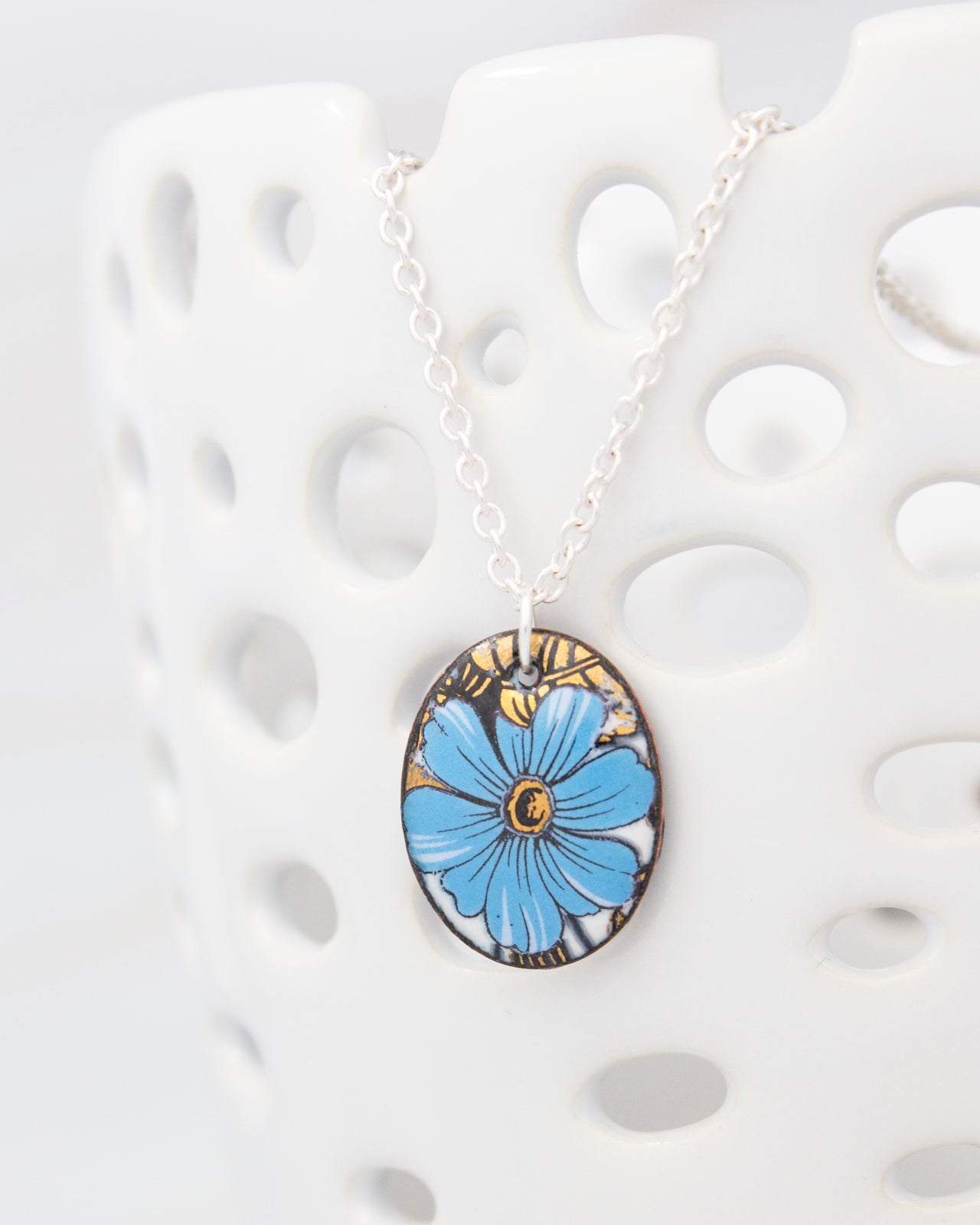 A necklace with a blue flower pendant is displayed against a white background.