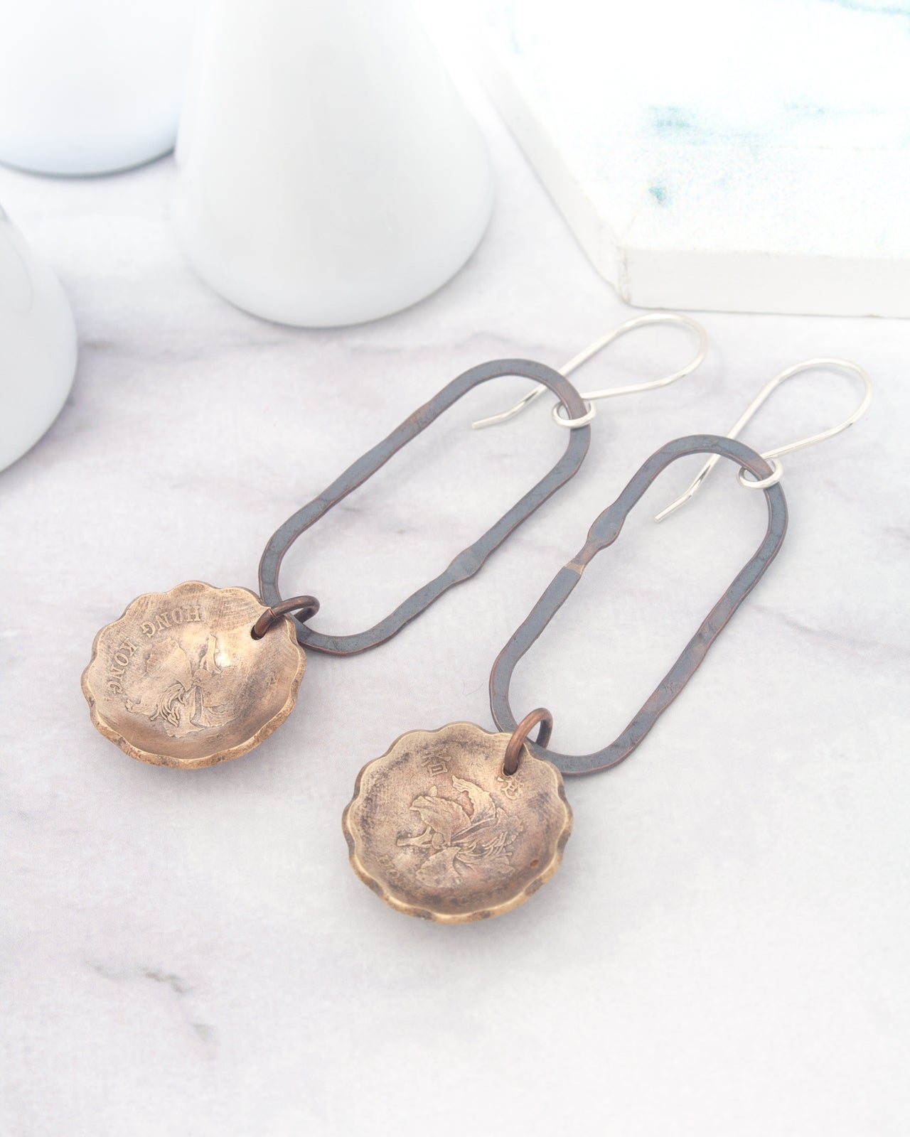 A pair of earrings with a metal frame and a round metal pendant, resting on a marble surface.