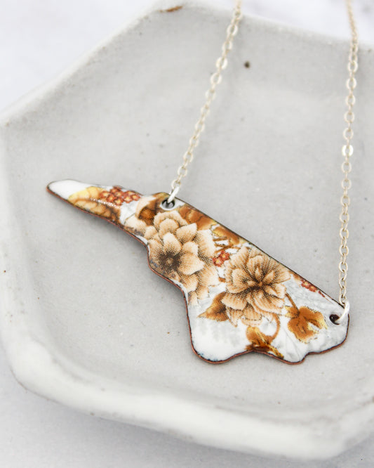 A necklace with a pendant in the shape of a flower, resting on a white plate.