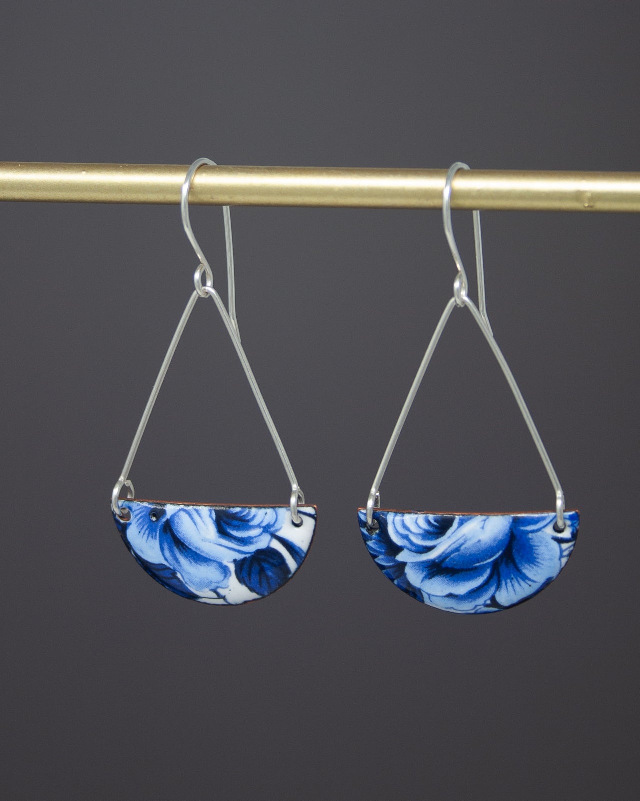 A pair of earrings with blue floral patterns hanging from a gold-colored metal hook.