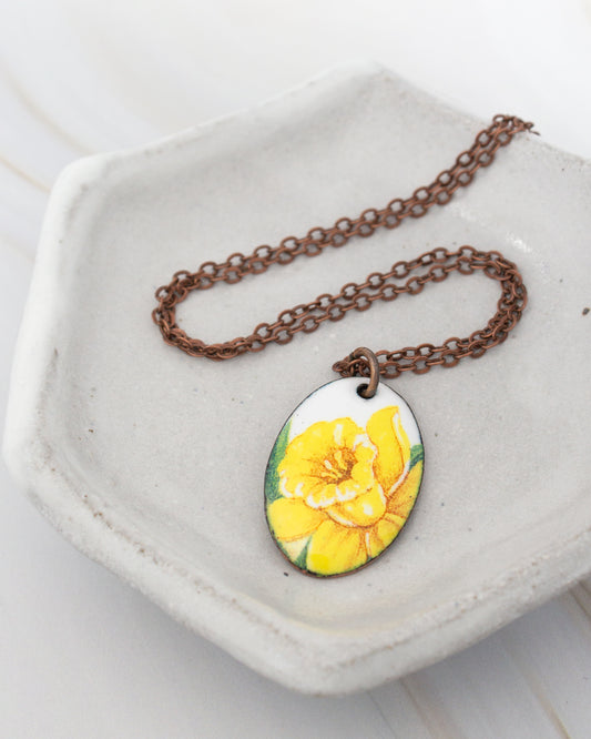 A necklace with a pendant featuring a yellow flower is displayed on a white plate.