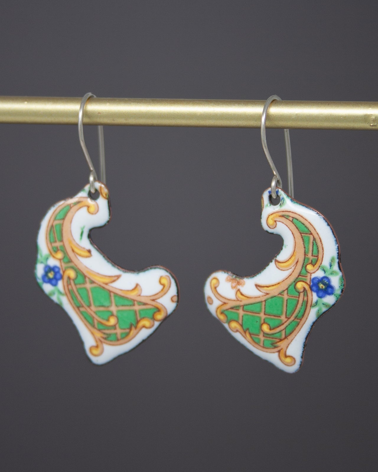 A pair of ornate earrings with intricate designs, hanging from a gold bar.