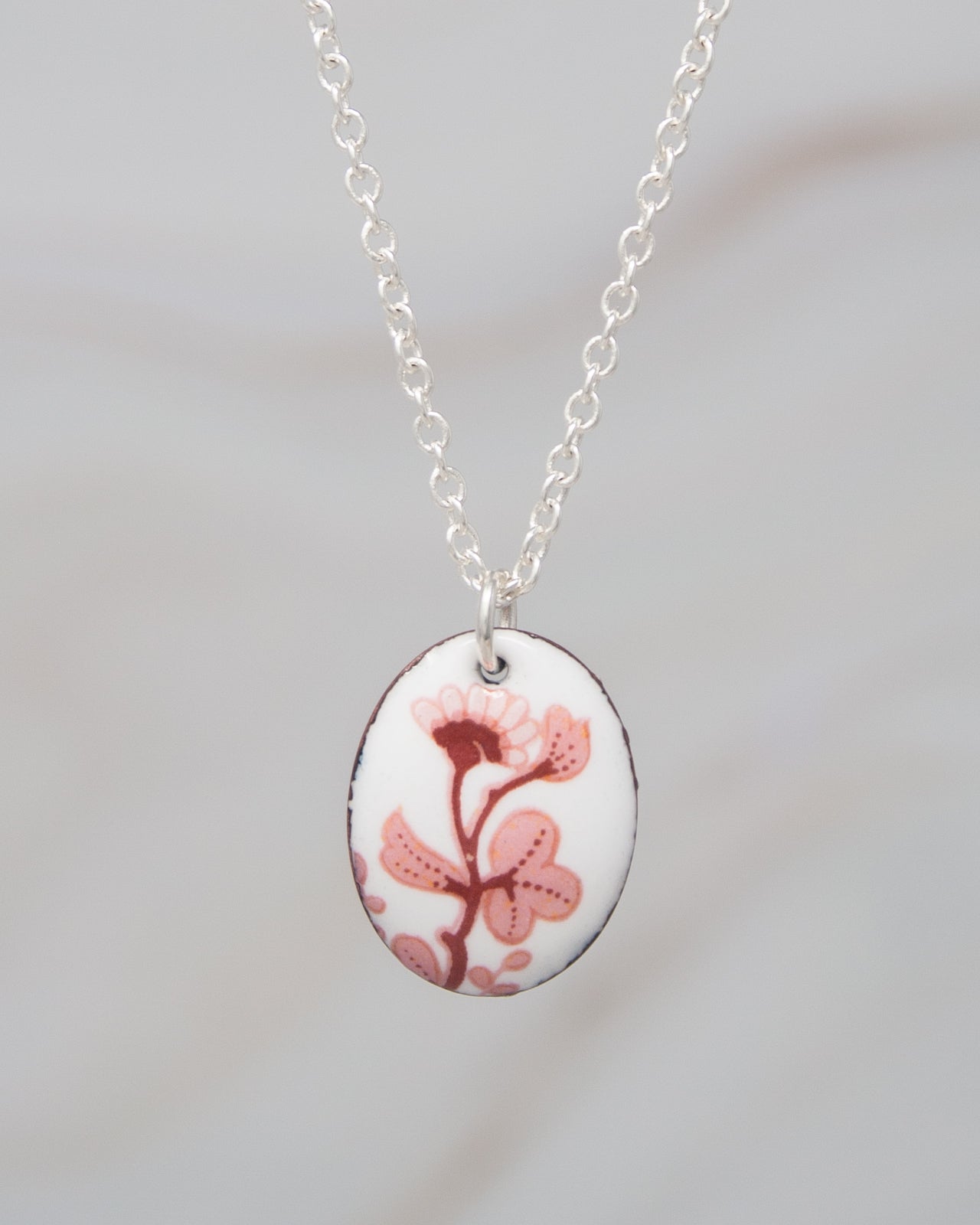 A necklace with a pendant featuring a floral design in pink and white colors.