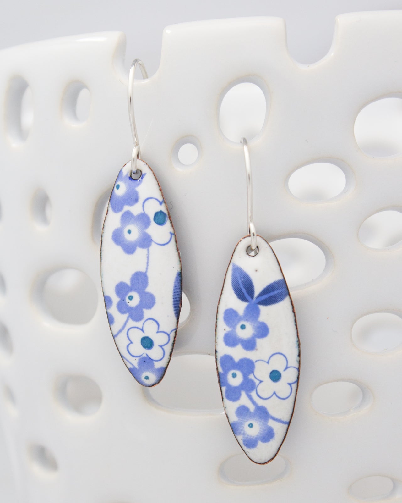 A pair of earrings with blue and white floral designs hanging from a hook.