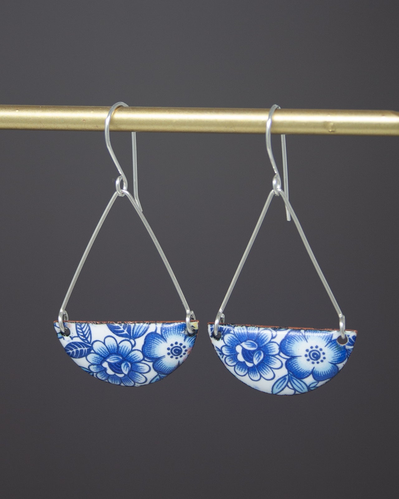 A pair of earrings with blue floral designs hanging from a gold-colored metal hook.