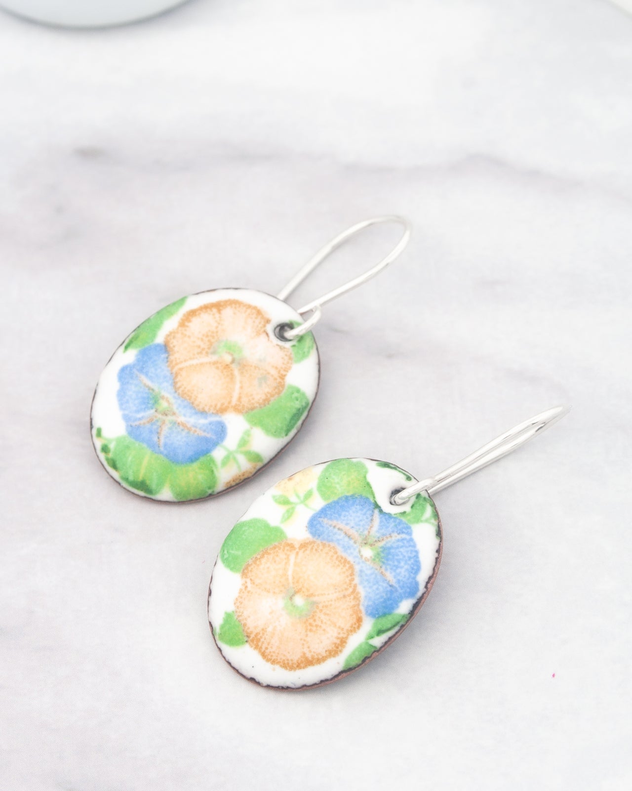 a pair of earrings with a floral design, featuring blue and orange flowers on a white background.