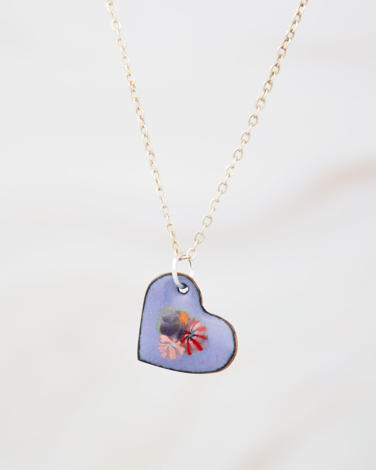 A delicate heart-shaped pendant with a floral design hangs from a chain against a plain white background.