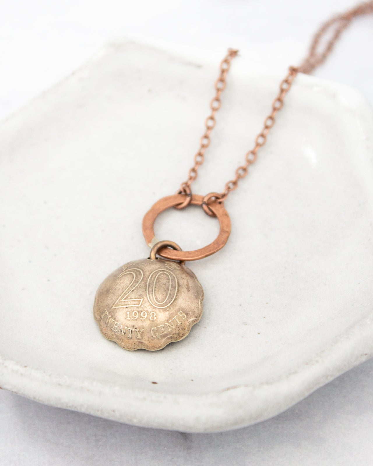 A necklace with a pendant featuring the number "20" and the year "1998" engraved on it.