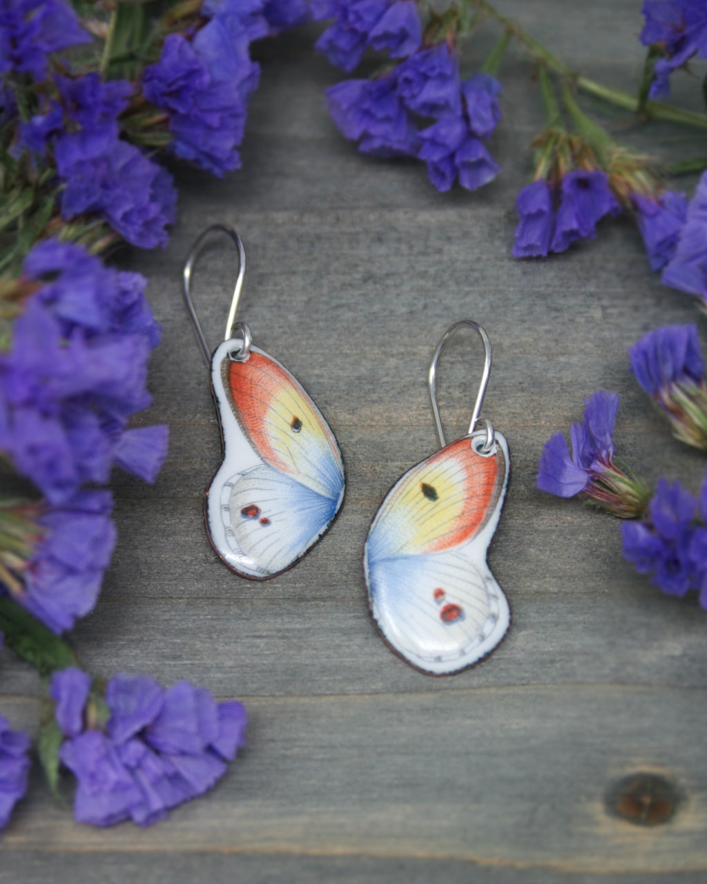 a pair of butterfly shaped earrings sitting on top of purple flowers