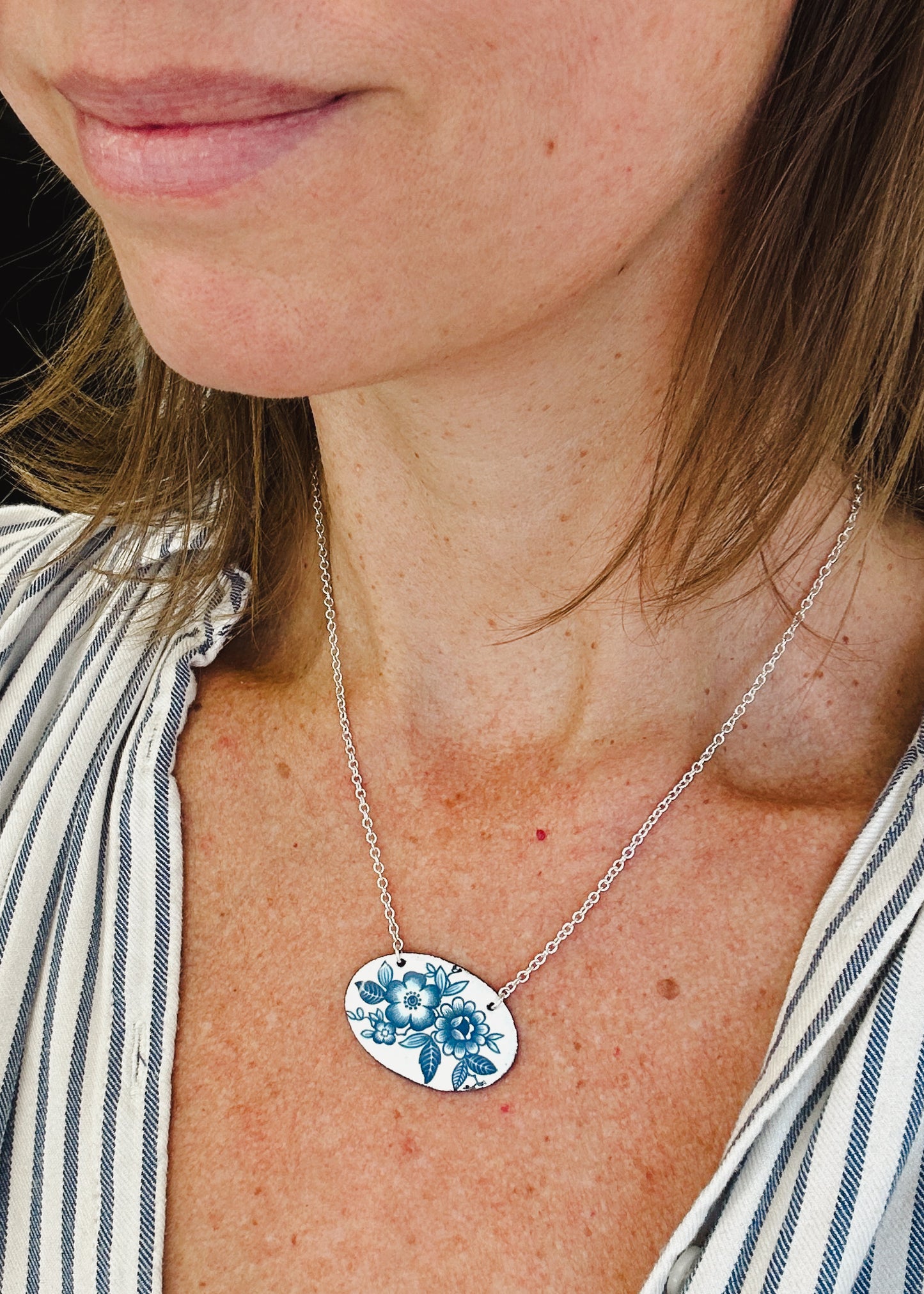 A close-up of a woman's neck and chest area, with a pendant necklace featuring a floral design.