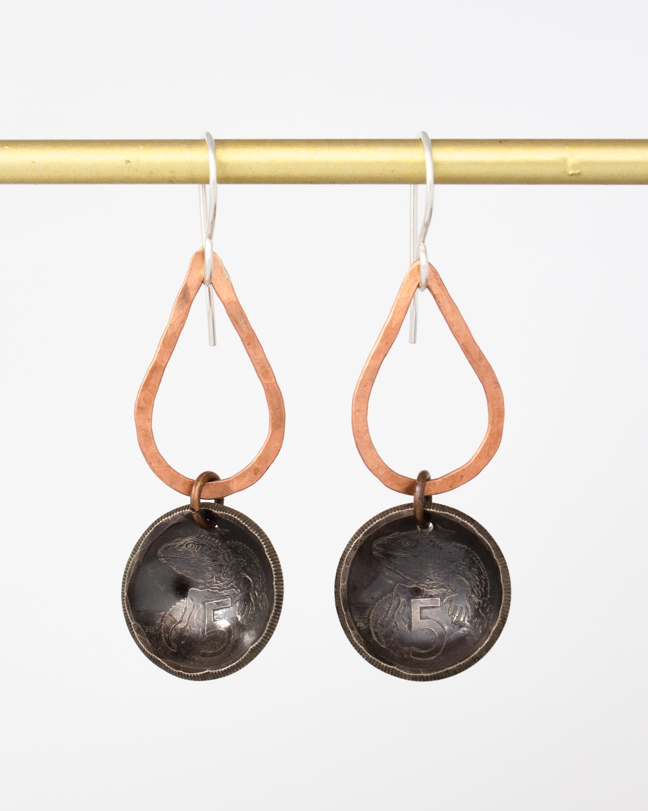 A pair of earrings with a copper-colored metal frame and a black metal pendant featuring a design.