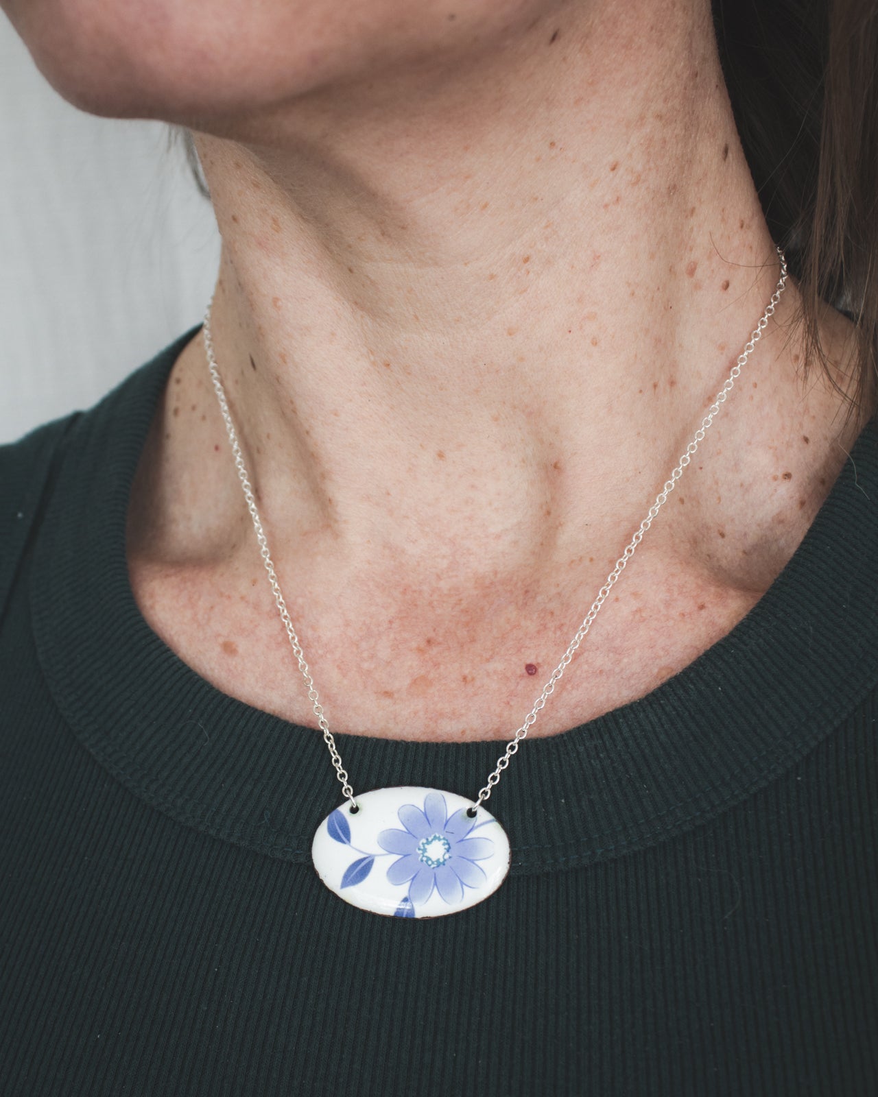 A woman wearing a necklace with a blue and white floral pendant.