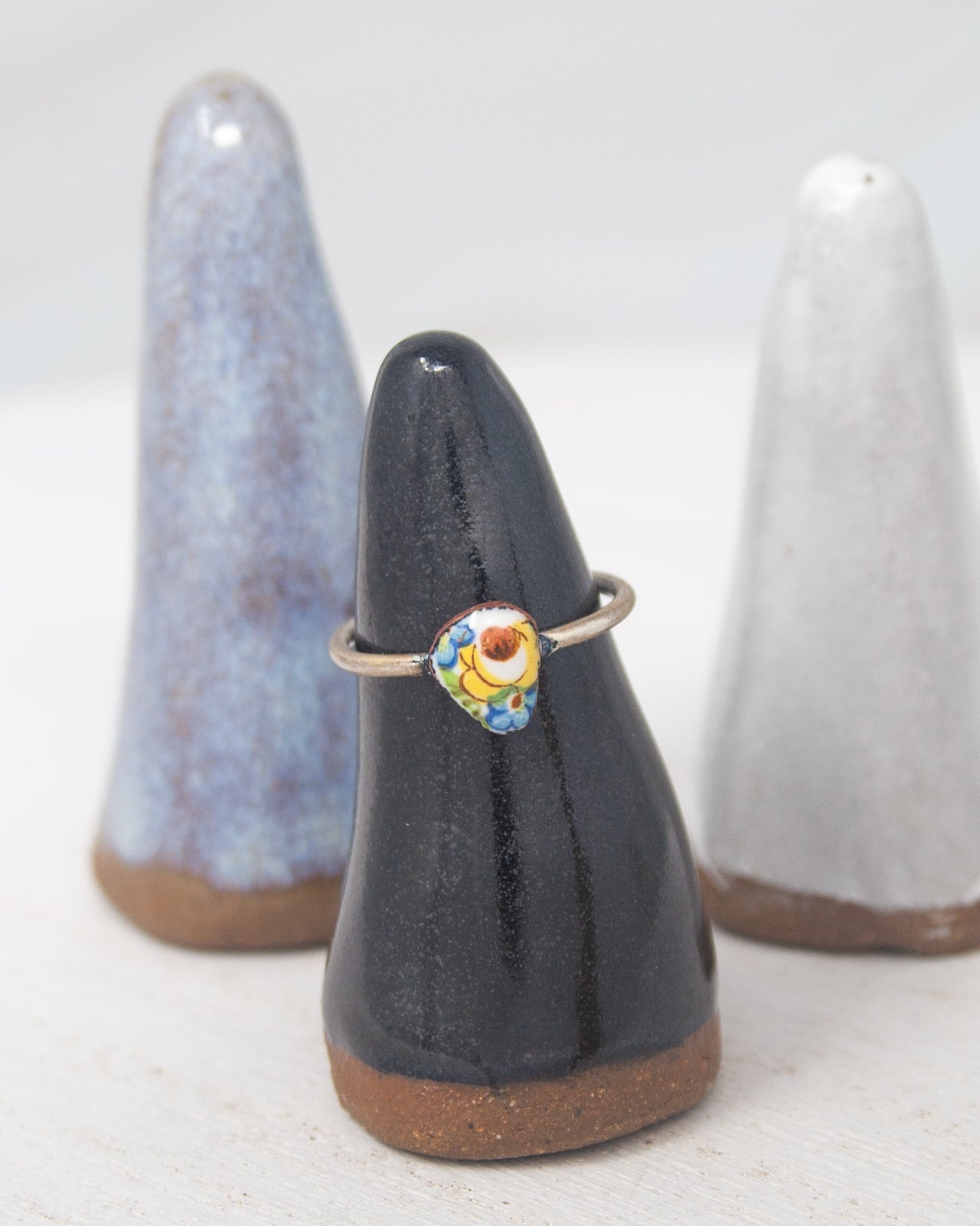 A ring is displayed on a black ceramic stand, with two white ceramic stands in the background.