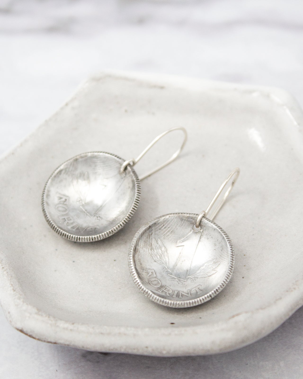 A pair of silver earrings with a coin-like design, resting on a white plate.