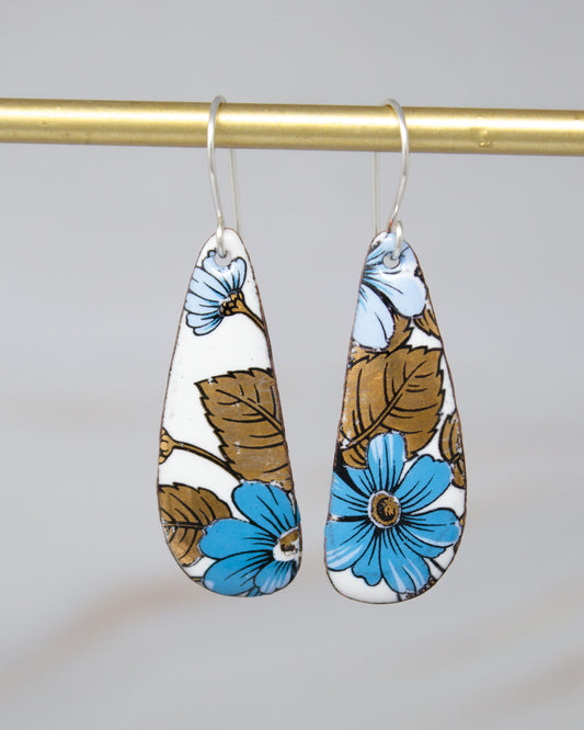 A pair of earrings with blue and brown floral designs hanging from a gold bar.