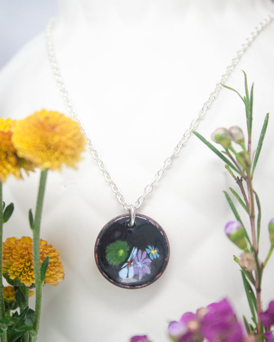 A necklace with a circular pendant featuring a floral design, surrounded by yellow flowers and purple flowers.