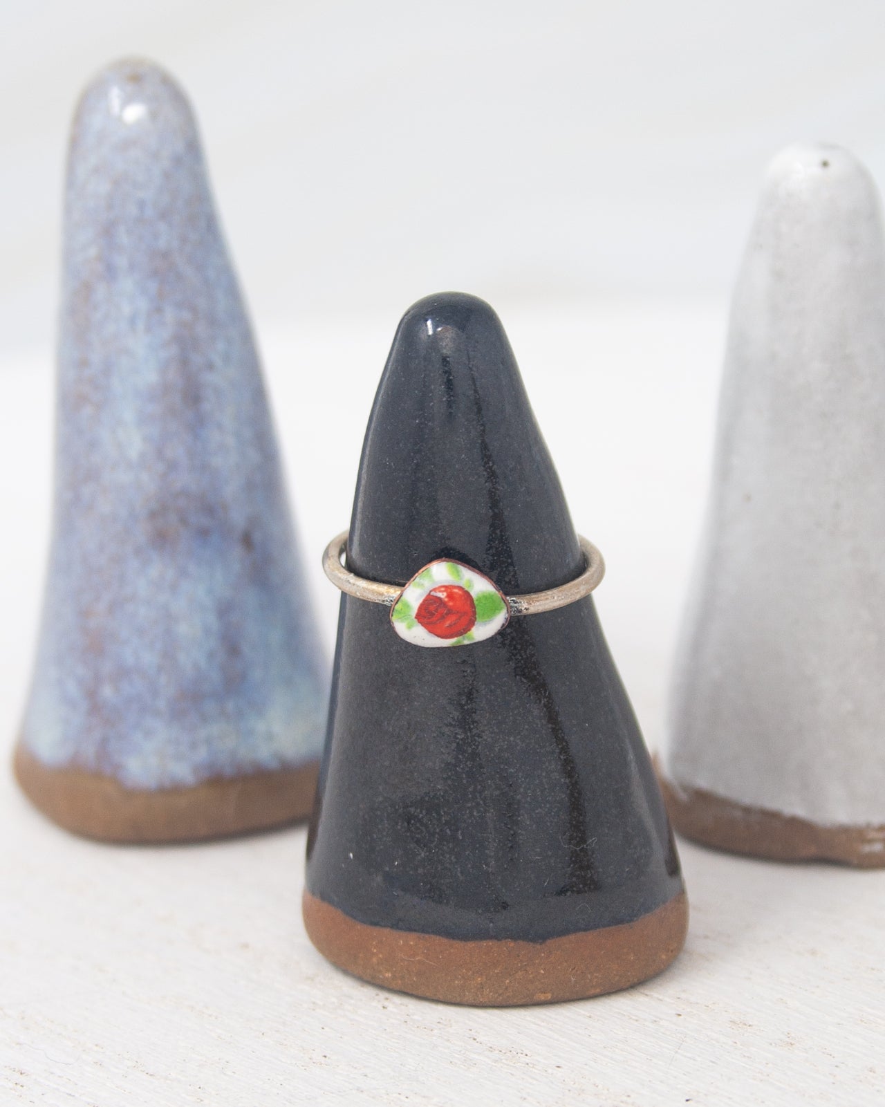 A black ceramic ring stand with a red flower design on it, placed between two white ceramic cone-shaped objects.