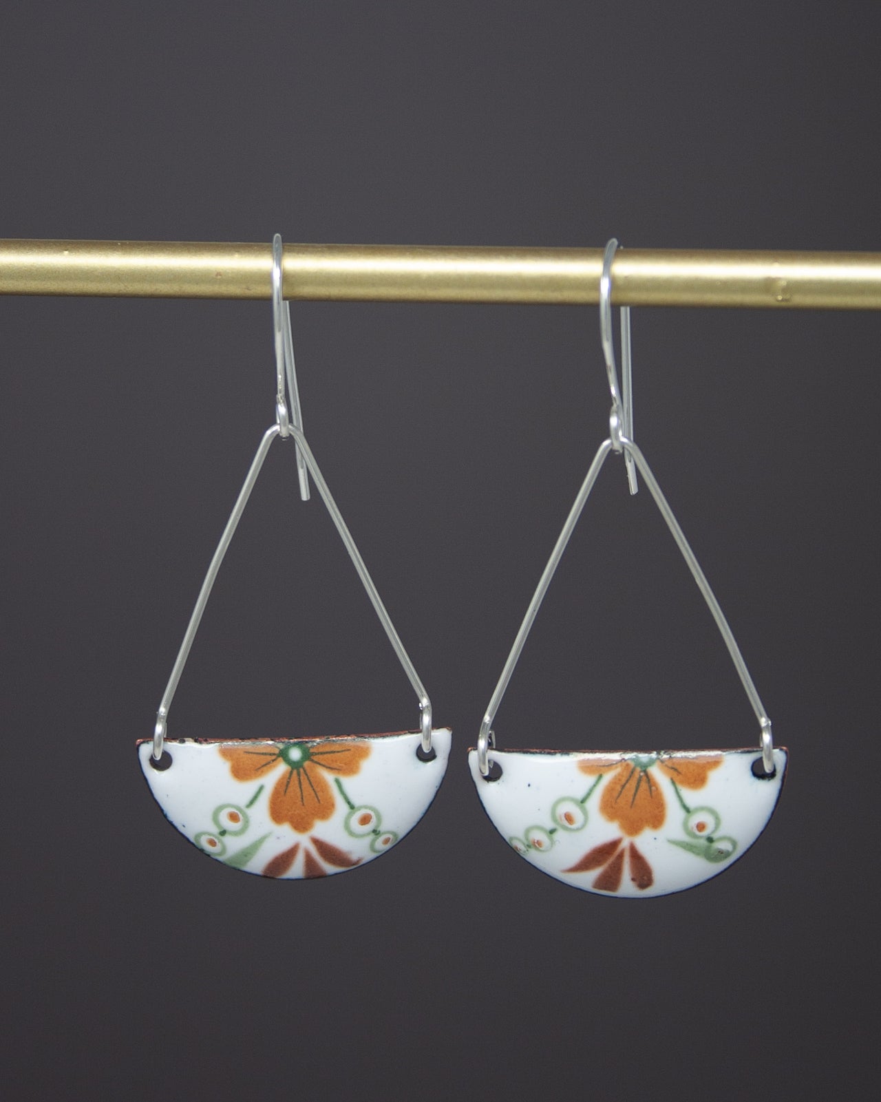 A pair of earrings hanging from a gold-colored metal hook against a dark background.