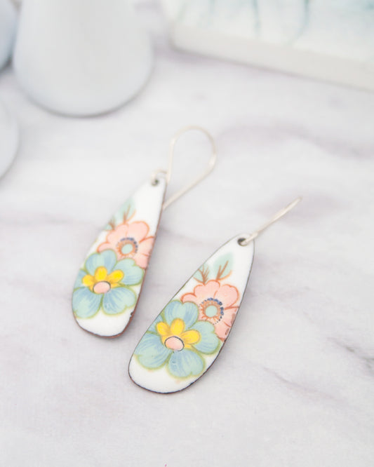 A pair of white earrings with colorful floral designs on them, resting on a marble surface.