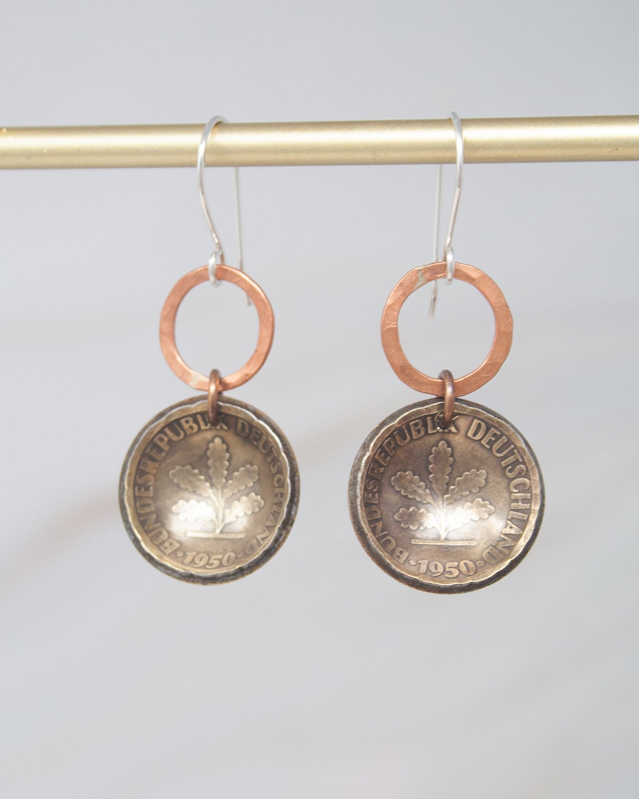 A pair of earrings made from two old coins, featuring a design that resembles a leaf.