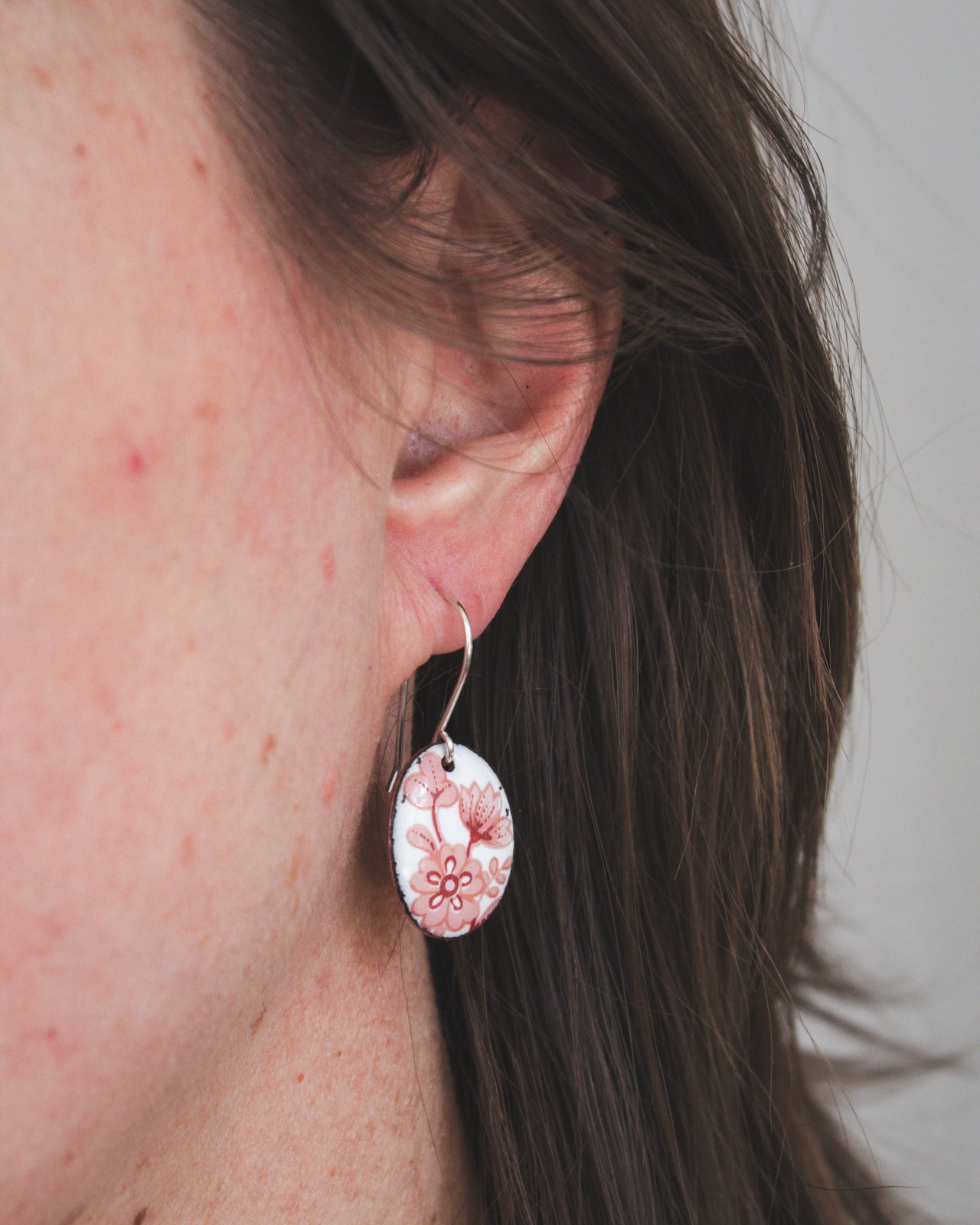 A close-up view of a person's ear wearing a pair of earrings with a floral design.