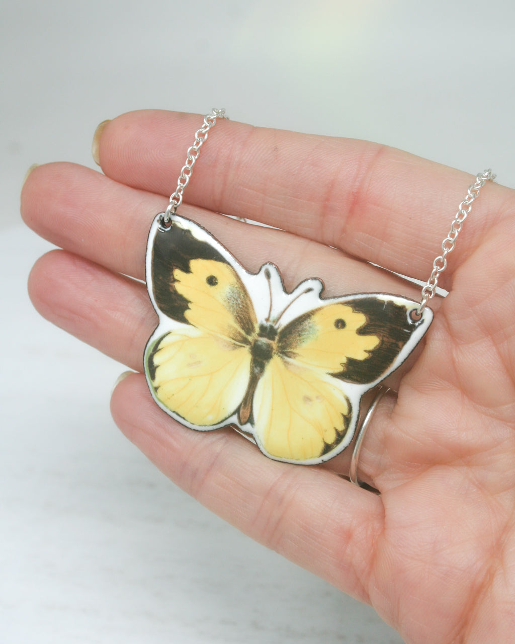 a hand holding a yellow and black butterfly pendant