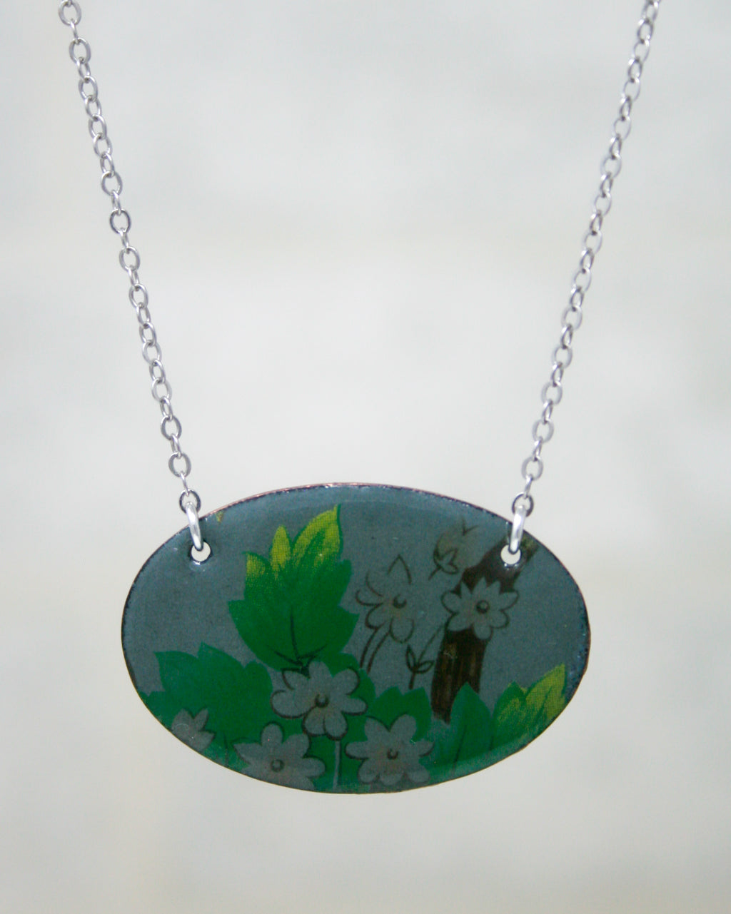 A necklace with a pendant featuring a floral design in shades of green and white.