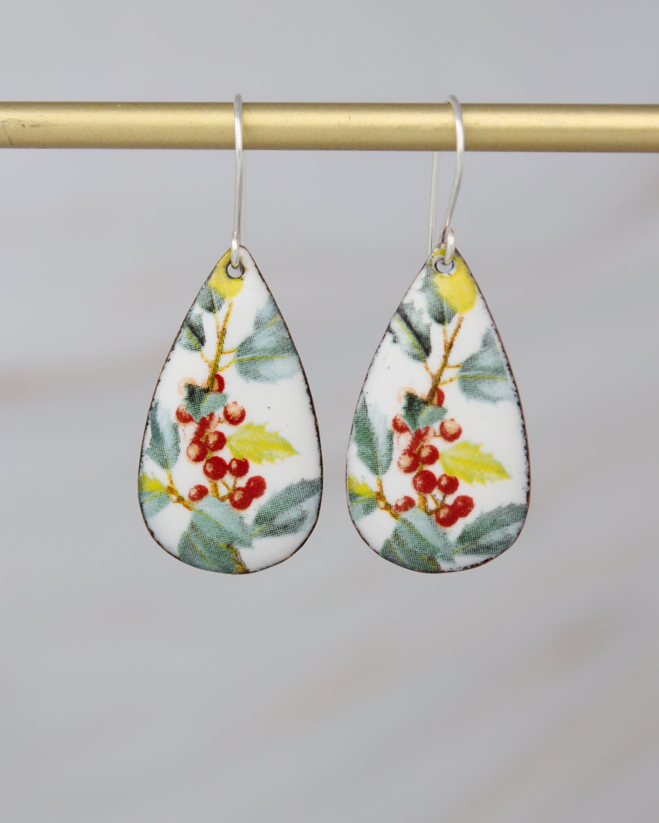 A pair of earrings with a floral design, featuring red berries and green leaves.