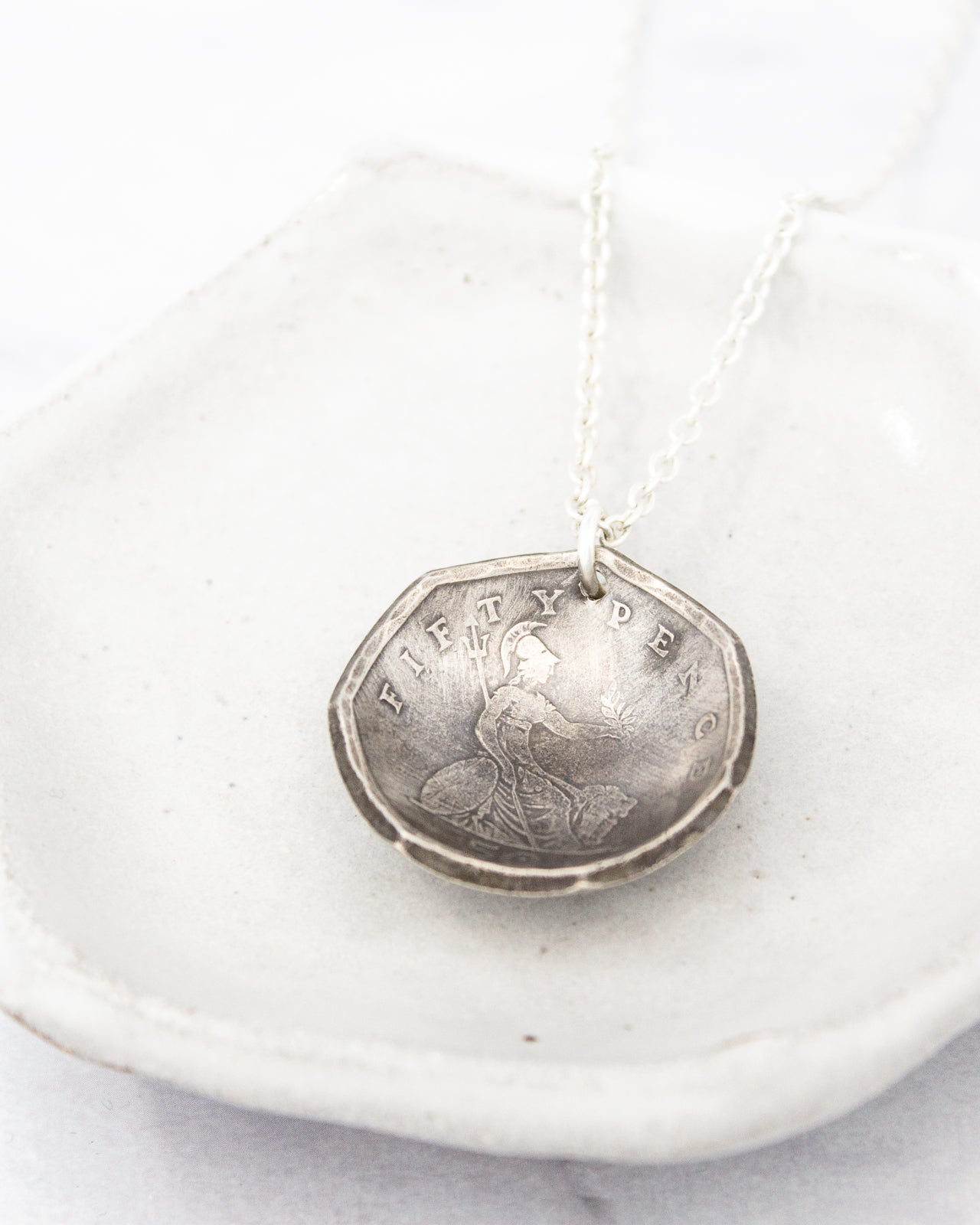A silver pendant necklace with a coin-like design on a white plate.