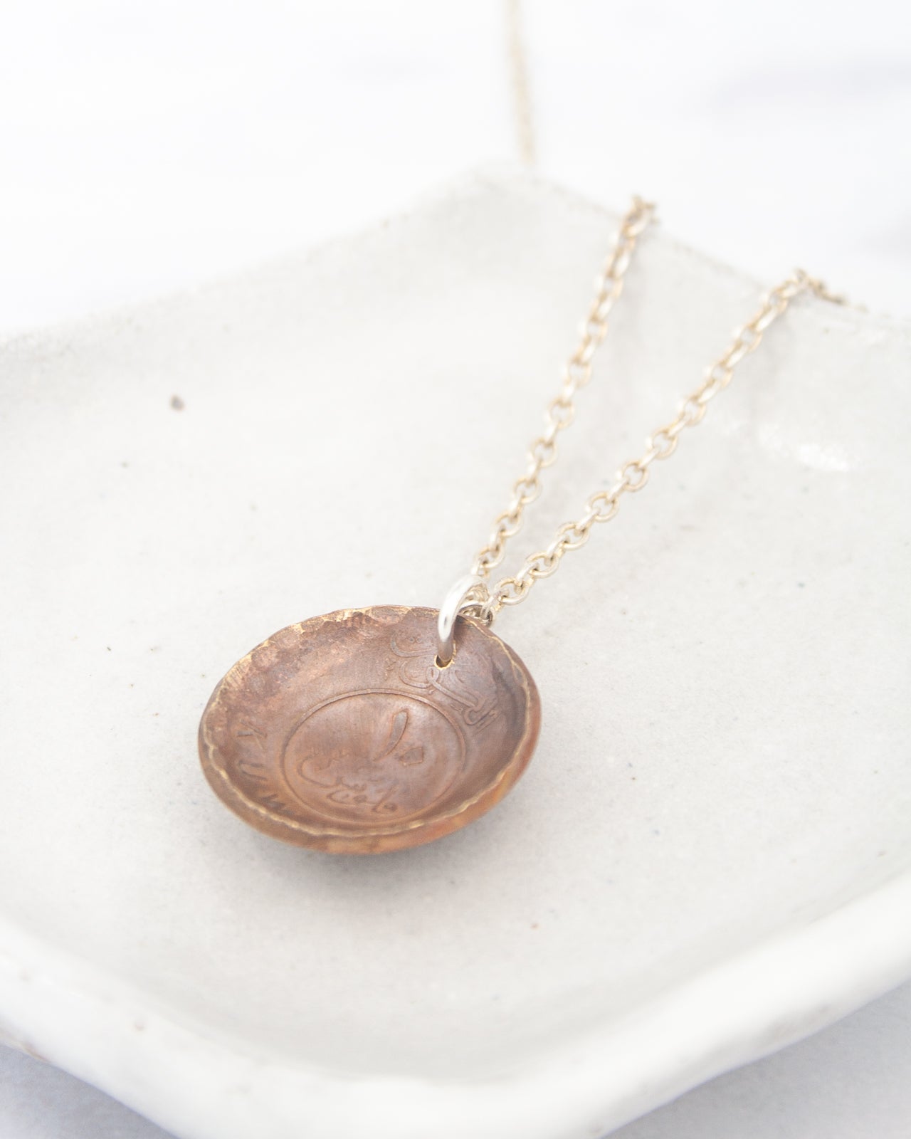 A necklace with a pendant in the shape of a small bowl or dish, hanging from a chain.