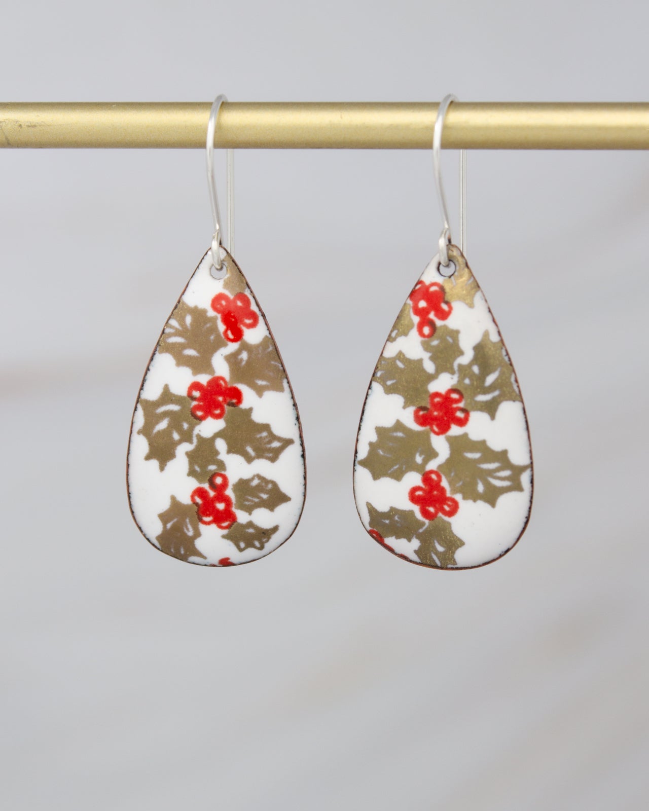 A pair of earrings with a floral pattern on a gold background, hanging from a gold bar.
