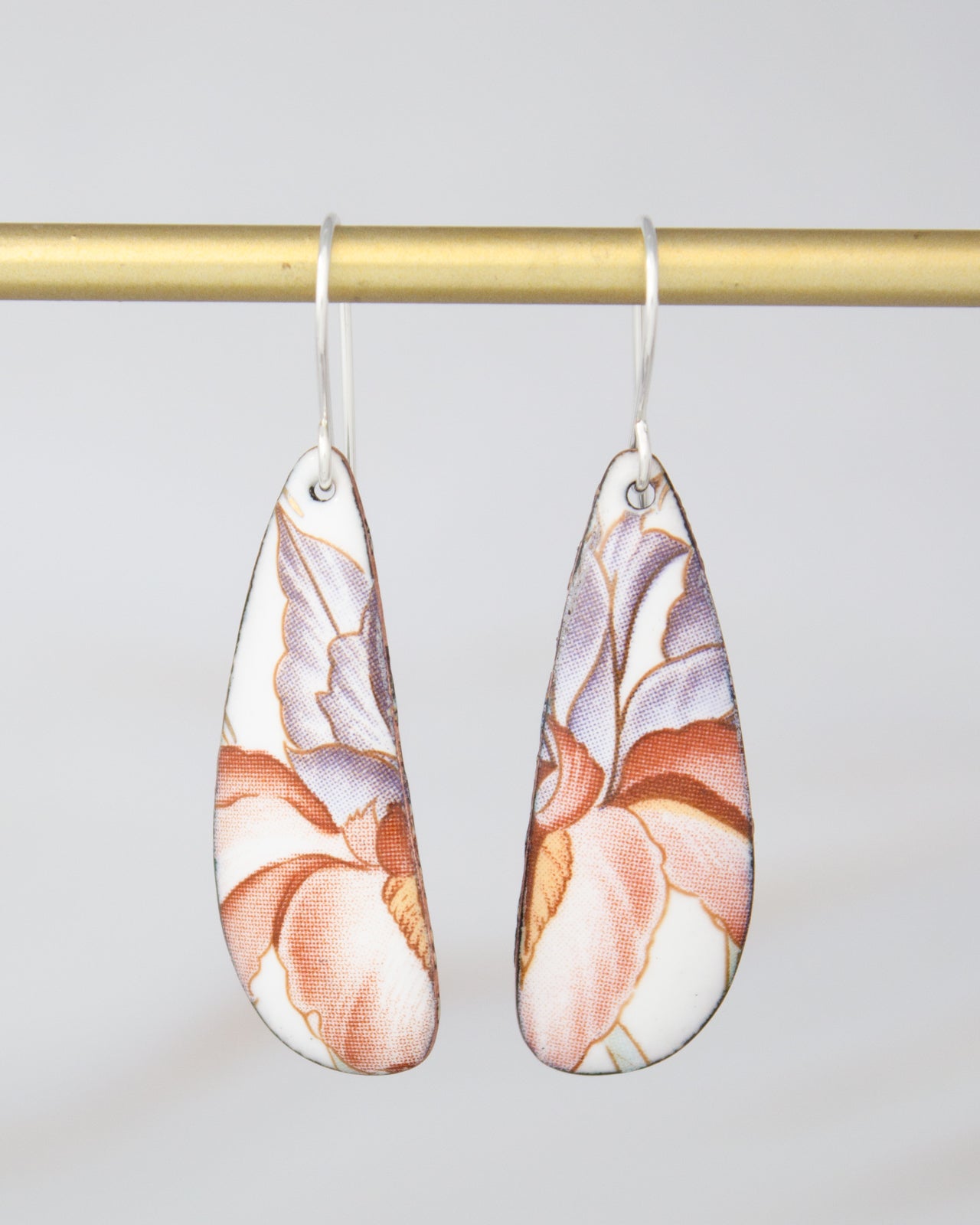 A pair of earrings with a floral design hanging from a gold-colored metal bar.