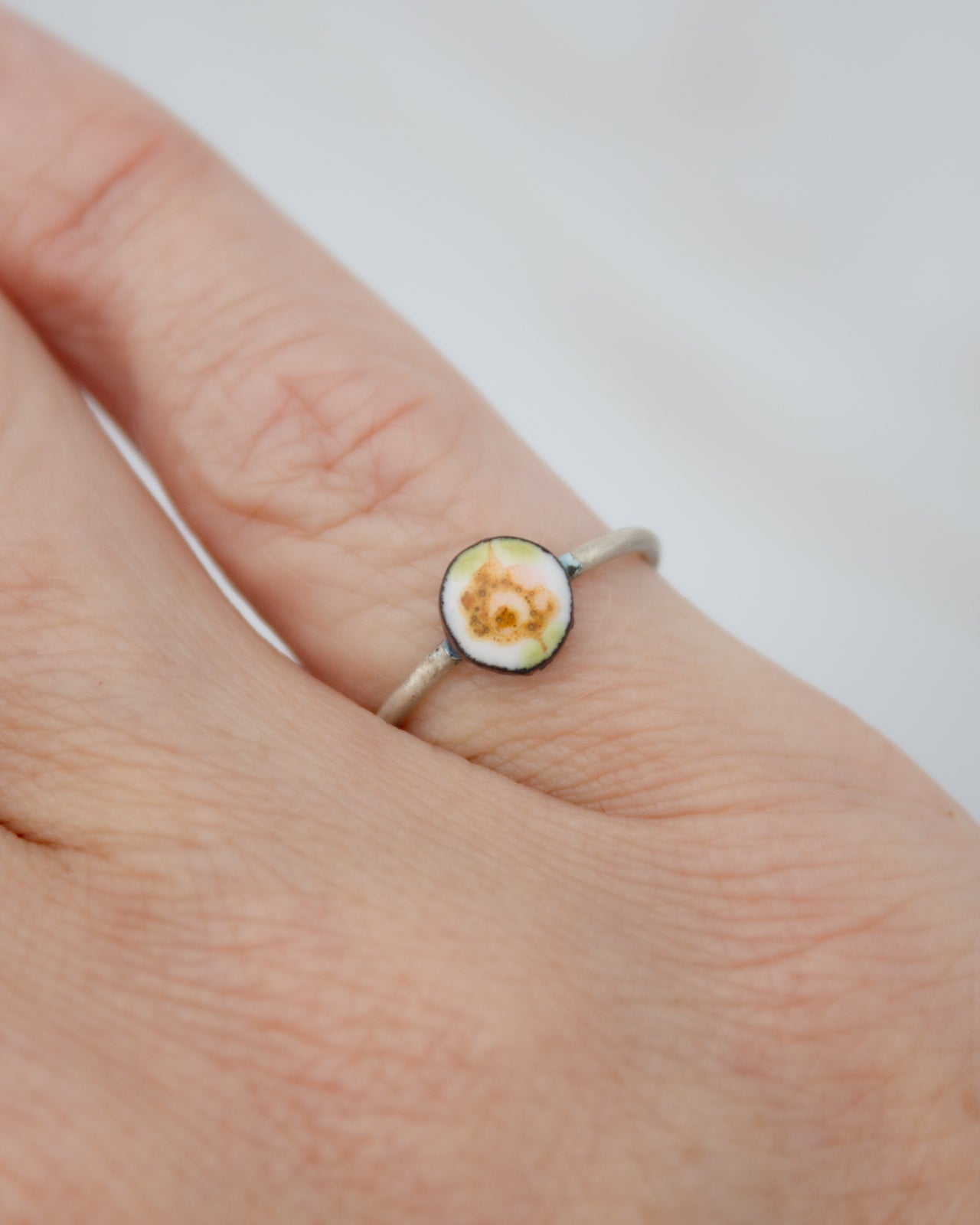 A silver ring with a small, round, and colorful object in the center, resting on a person's finger.