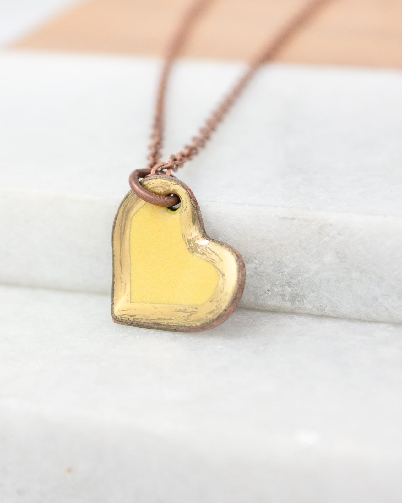 A heart-shaped pendant with a yellow background is hanging from a chain.