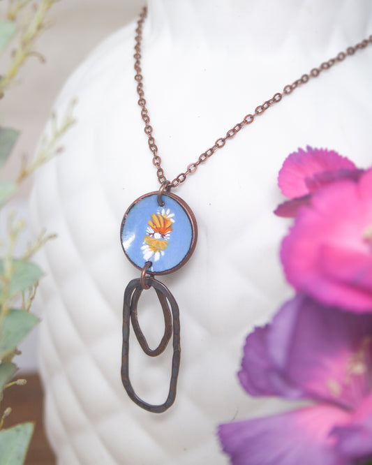 A necklace with a blue circular pendant featuring a floral design, hanging from a chain.