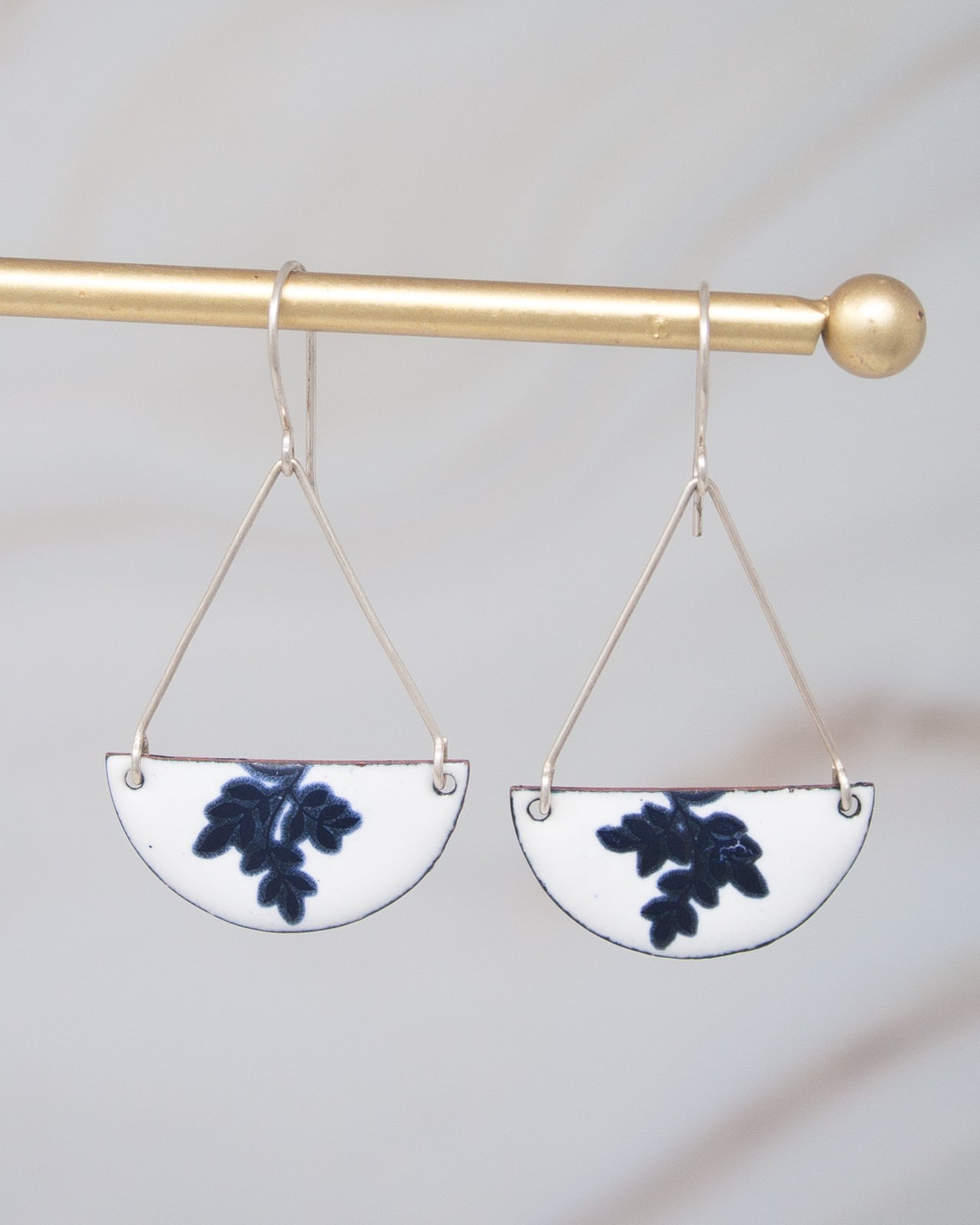 A pair of earrings with a white and blue floral design hanging from a gold-colored metal hook.