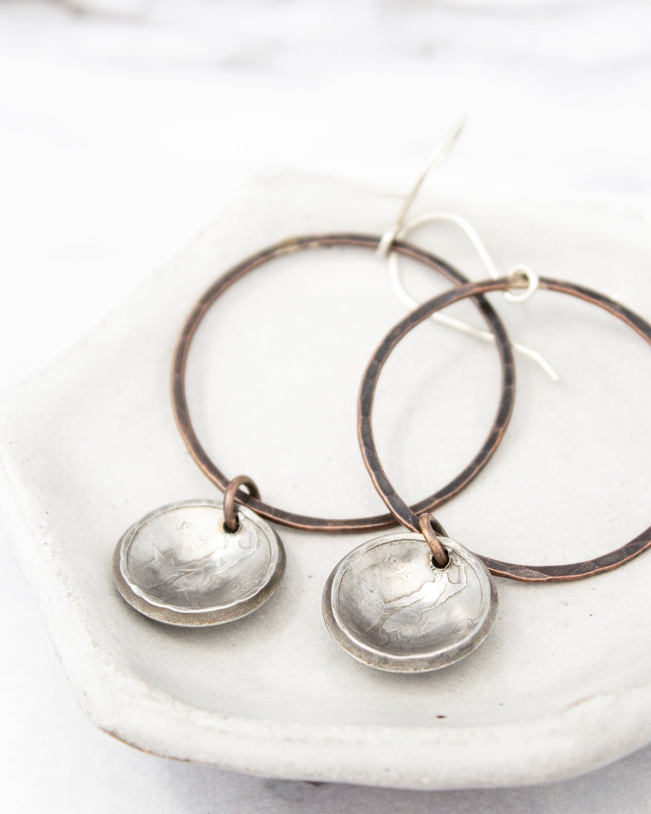 A pair of silver earrings with circular pendants, resting on a white plate.