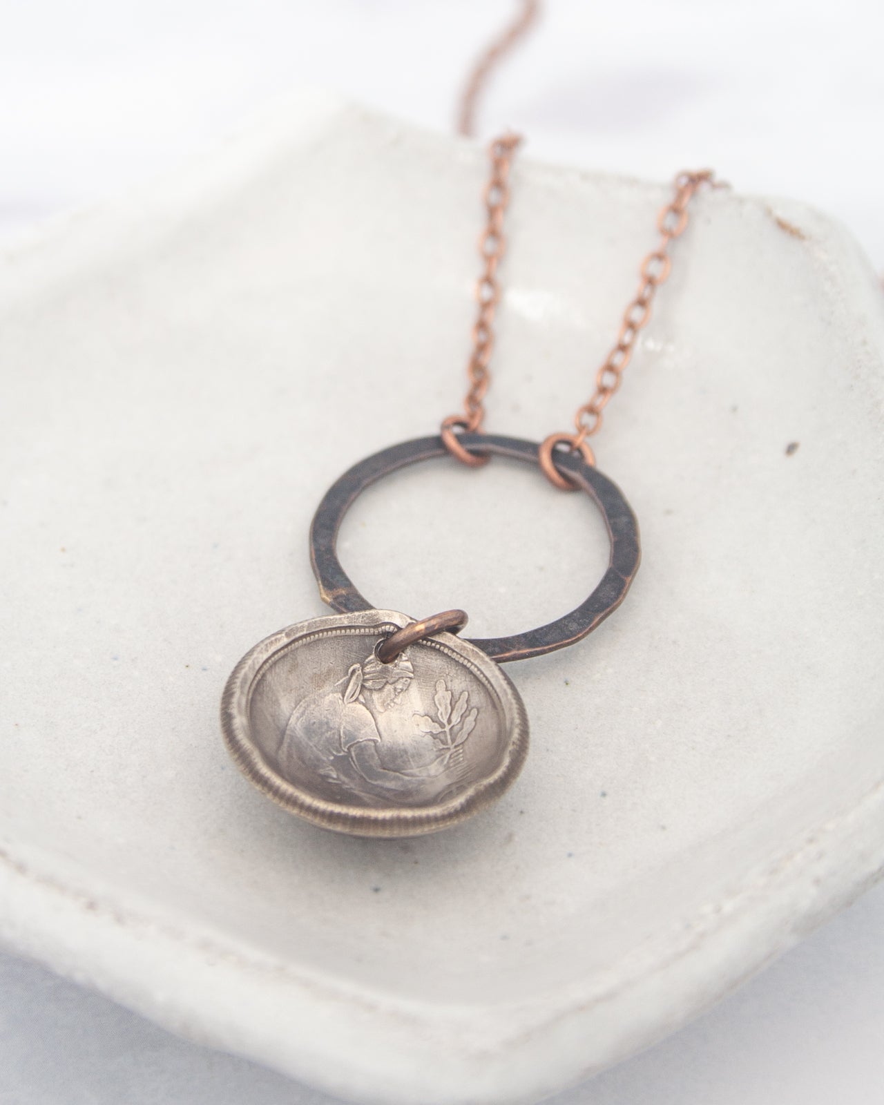 A silver-colored pendant with a circular design hangs from a chain, resting on a white surface.