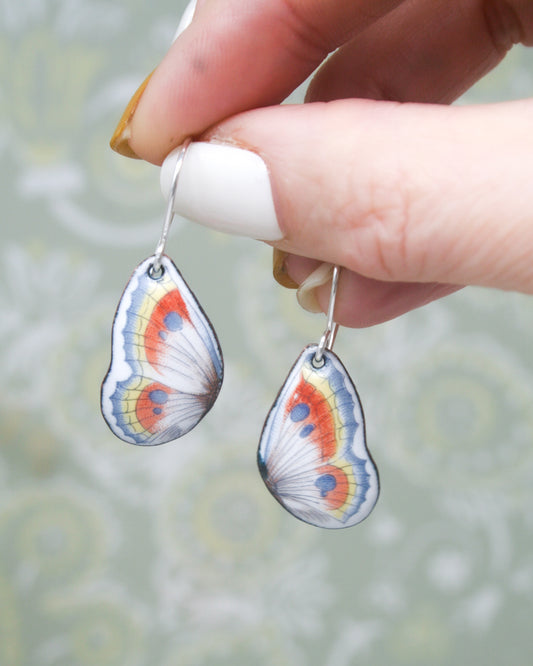 a hand holding a pair of earrings with a butterfly on it