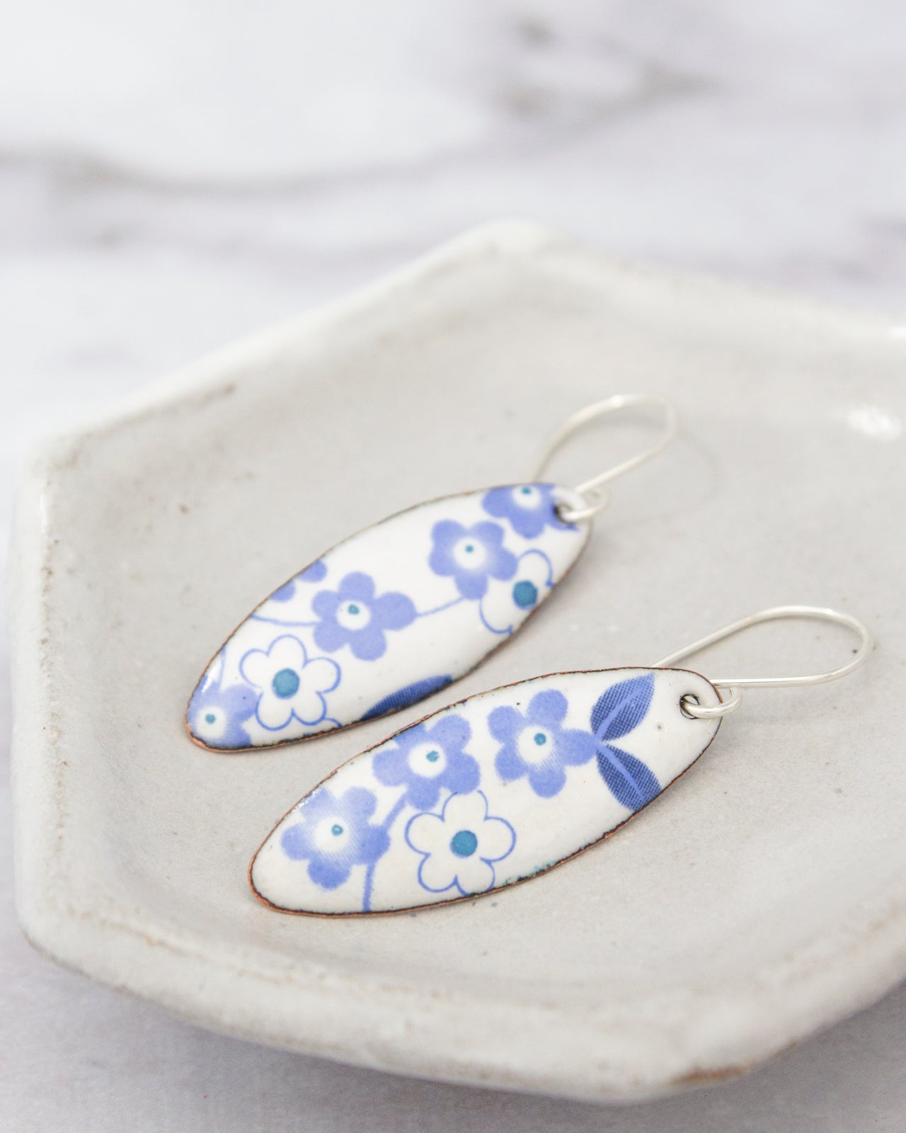 A pair of blue and white floral earrings are displayed on a white plate.