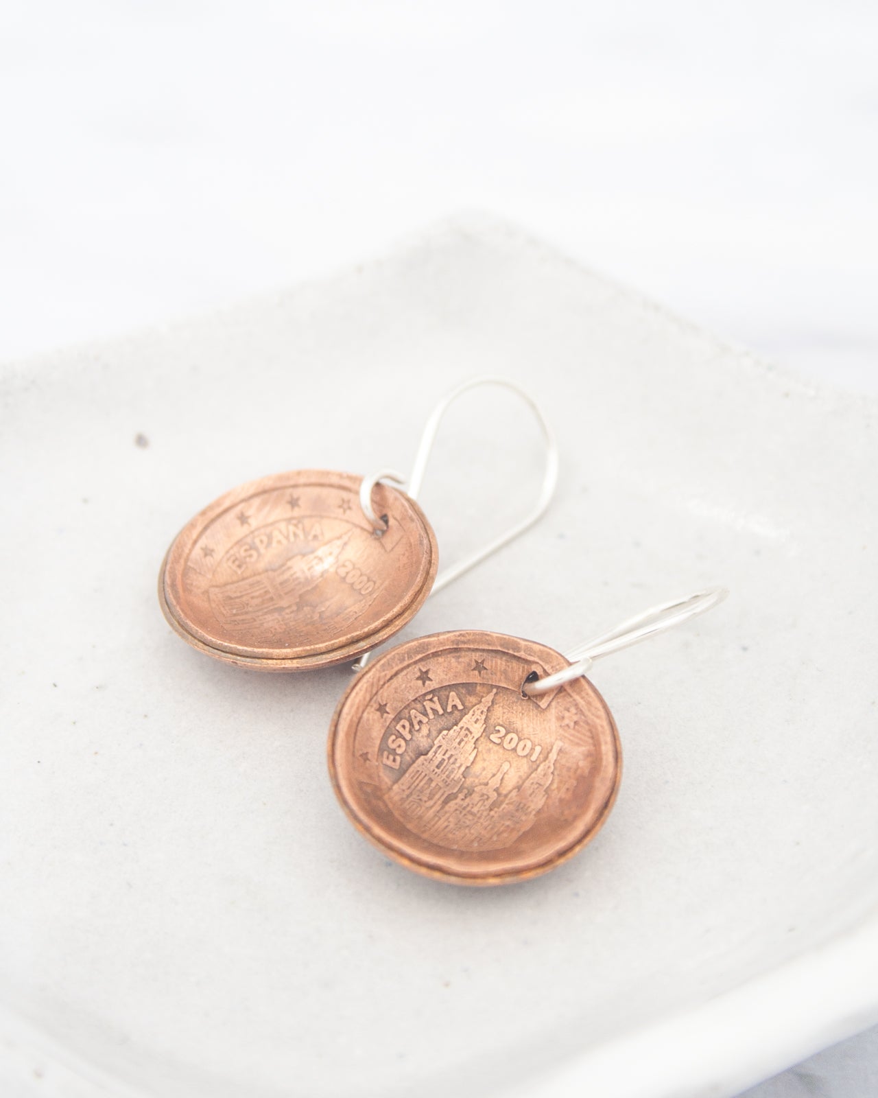 a pair of earrings made from Spanish coins, with the text "ESPAÑA 2001" visible on the coins.