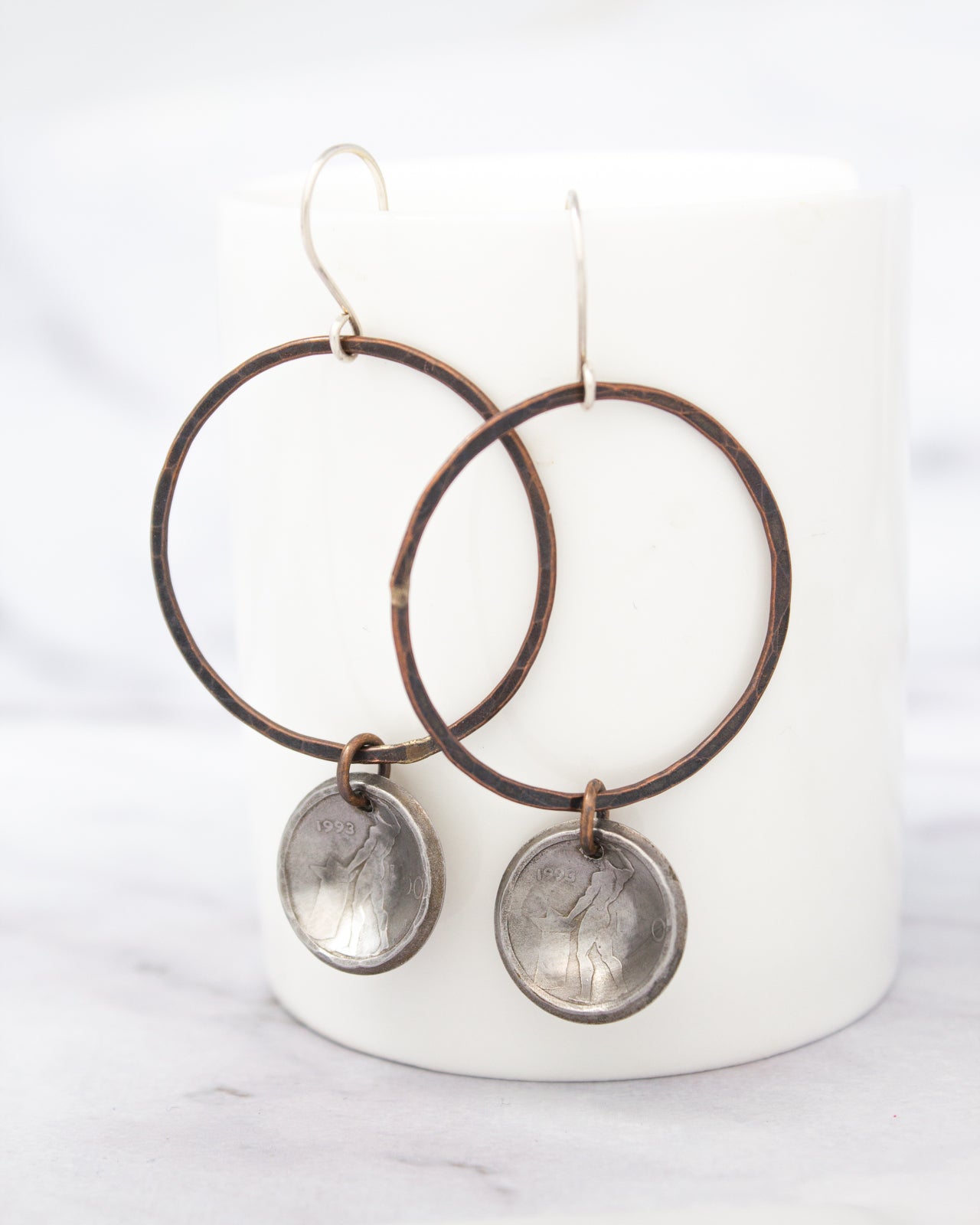 A pair of earrings with a circular metal charm hanging from each hoop, set against a white background.