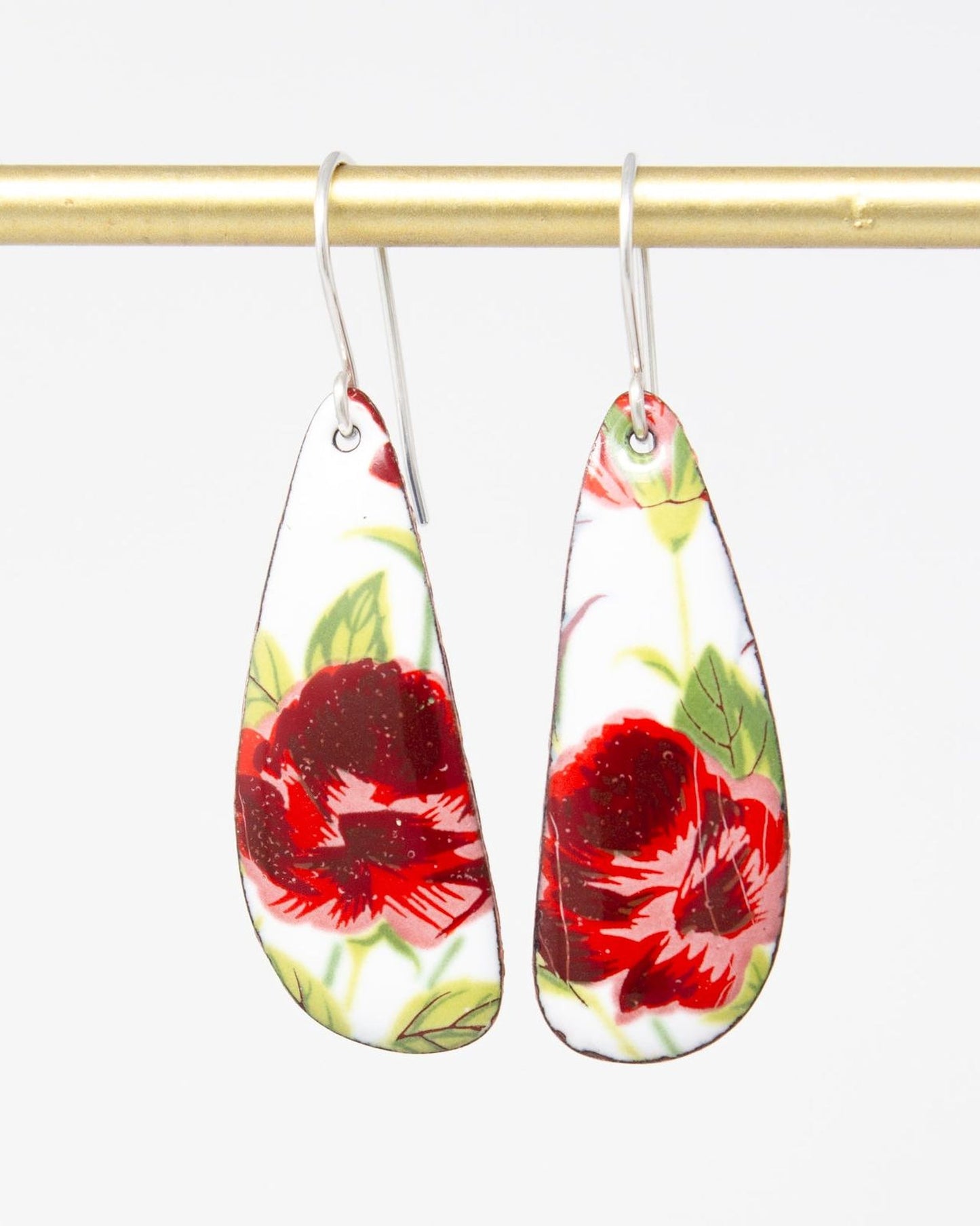 A pair of earrings with a floral design, featuring red and green flowers against a white background.