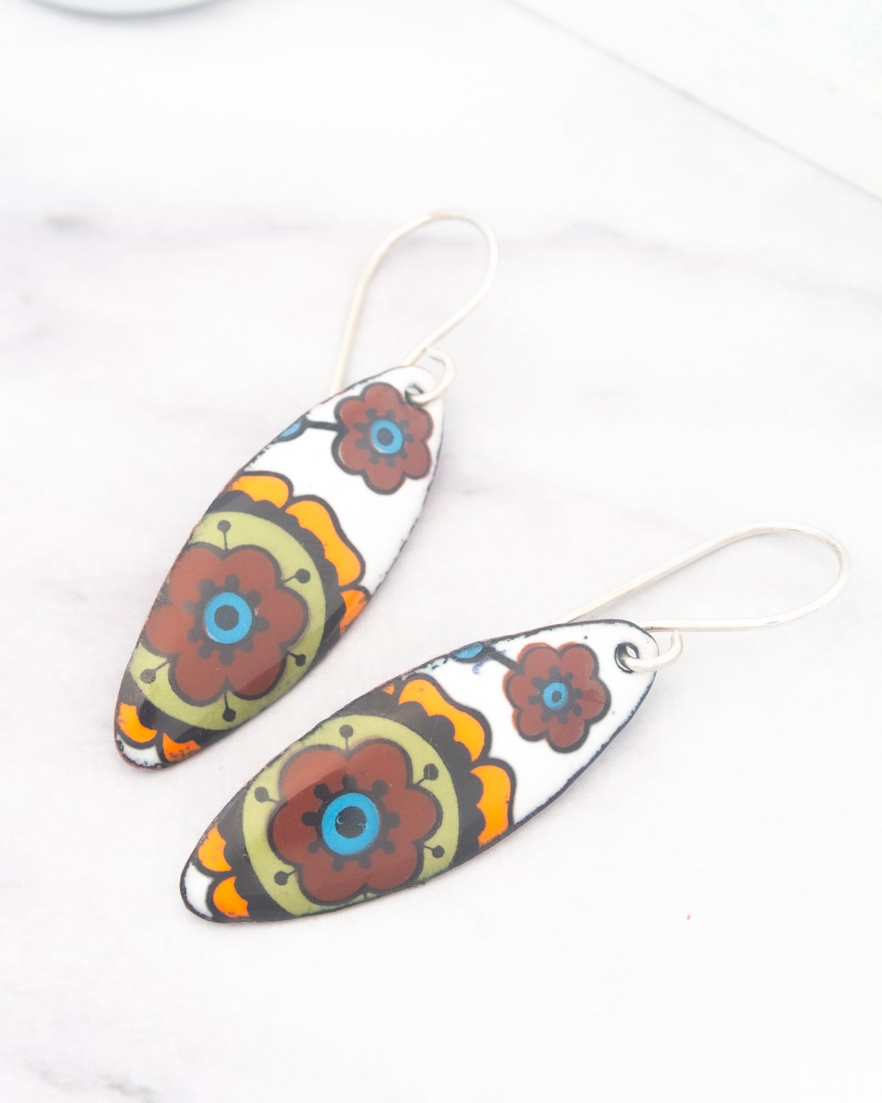 A pair of colorful earrings with floral designs on a white marble surface.