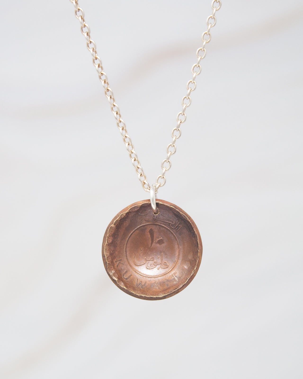 A necklace with a pendant made of a copper-colored metal, possibly a coin, hanging from a chain.