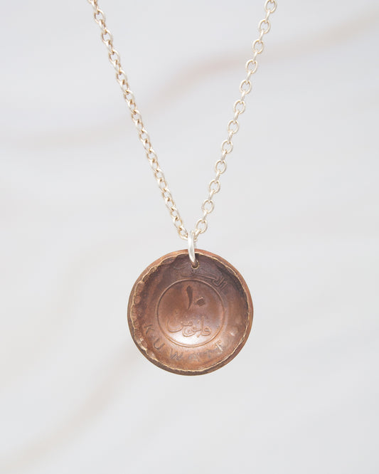 A necklace with a pendant made of a copper-colored metal, possibly a coin, hanging from a chain.