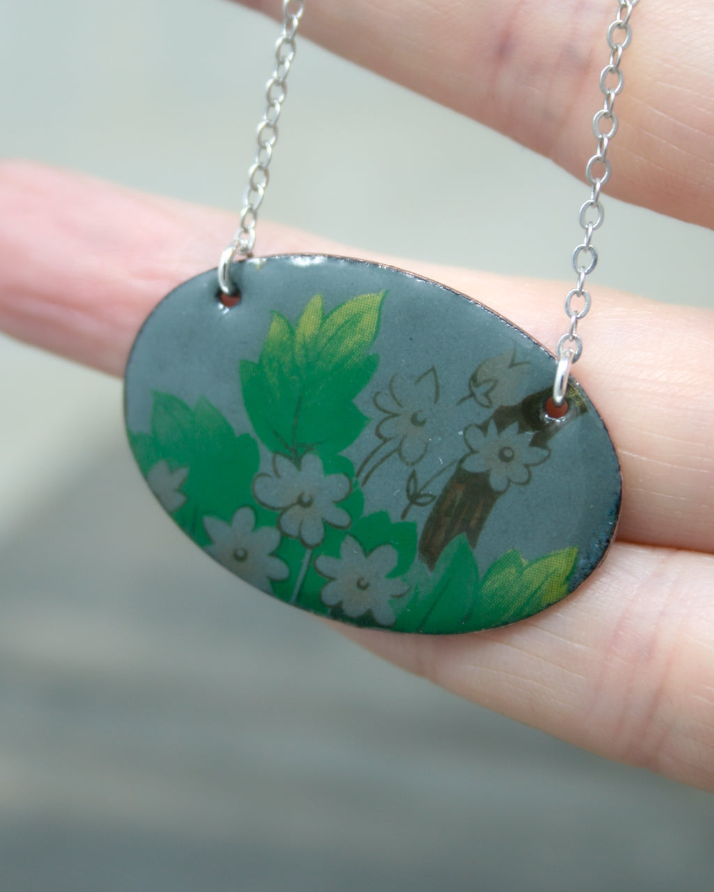 A hand holding a pendant necklace with a floral design on it.